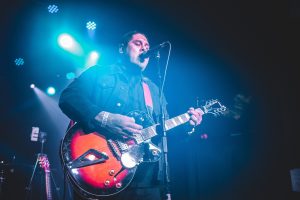 Musician Danny Attack performing on stage with a guitar and mic