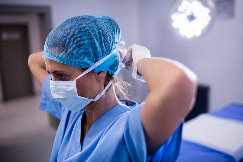 Female nurse tying surgical mask in operation theater Female nurse tying surgical mask in operation theater