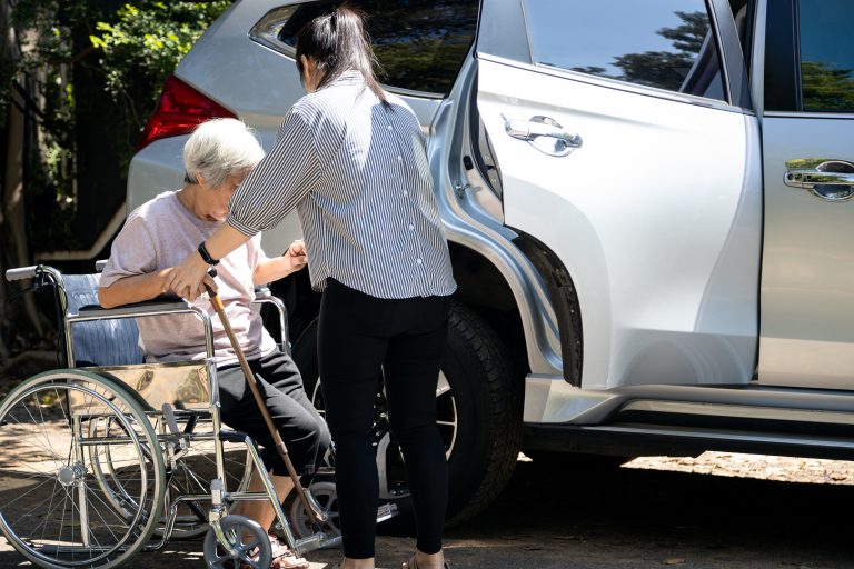 Asian female caregiver helping disabled elderly woman in wheelch
