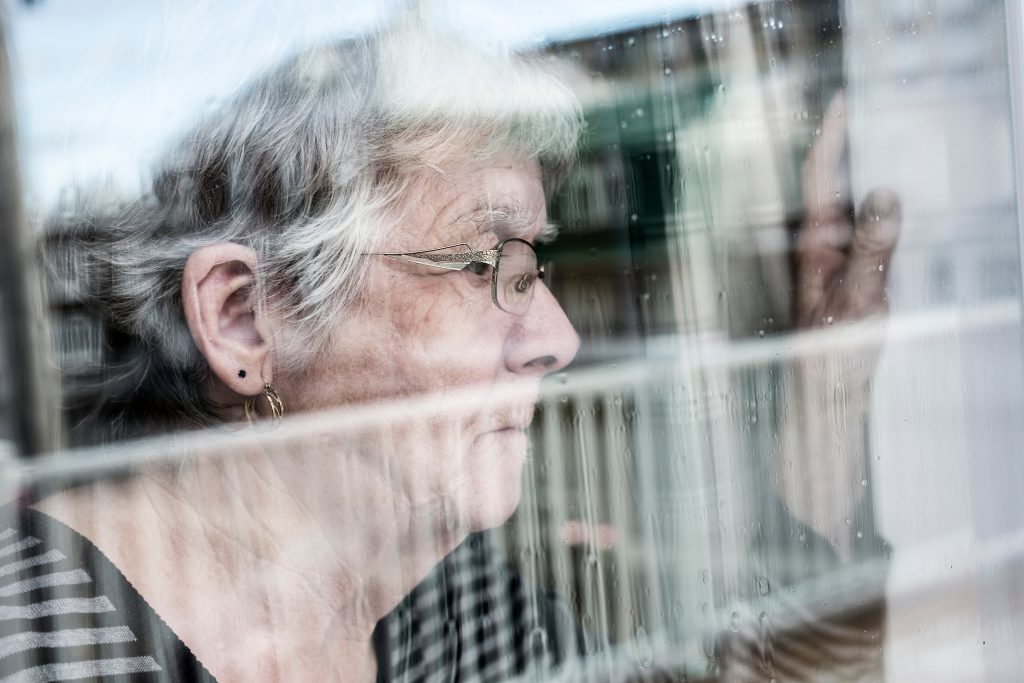 A Senior woman looking out through a window like depress