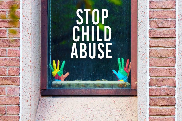 Stop child abuse written on the window of a building with mockup model child hands.