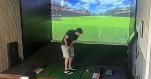 A golfer takes a swing at a golf ball at Pin Seeker Indoor Golf’s simulator