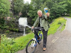 Travel guru Rick Steves on a bicycle holding up one of his travel guides.