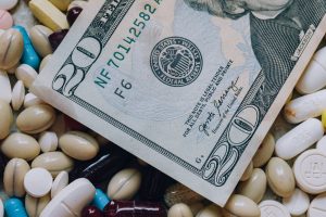 Photo of a 20 US dollar bill among pills of many shapes and colors that could probably be used to illustrate the economics of the pharmaceutical industry in the United States of America.